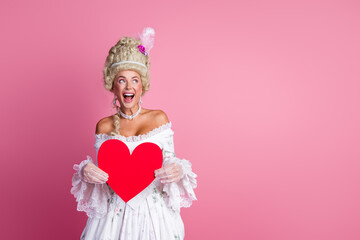 Sophisticated woman dressed as a baroque aristocrat holding a red heart against a pink background...