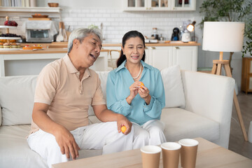 Obraz premium Asian senior couple playing toss ping pong ball to the cup in the living room at home on weekend after retirement. Healthy insurance concept
