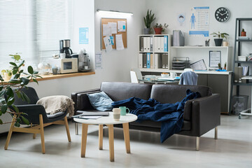 Bright living room with cozy grey couch with blue blanket, wooden coffee table with coffee cups,...
