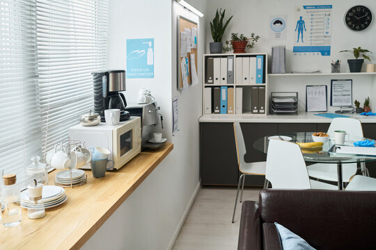 Stylish office kitchen with coffee maker, microwave, and neatly arranged dishes on wooden countertop. Notice board with documents and shelves with files and plants enhance functionality