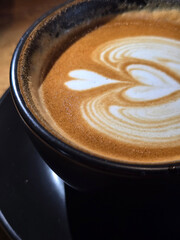 A close-up view of a beautifully crafted heart-shaped latte art on a frothy cup of coffee served in a matte black cup and saucer.