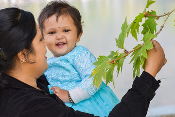 Asian Indian mother holding her child baby girl and showing green leaf to her. beautiful and cute daughter smiling. early learning, travel, parenting, kids fashion, healthy child concept