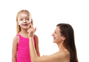 Smiling mother applying sun protection product onto her daughter's cheeks on white background