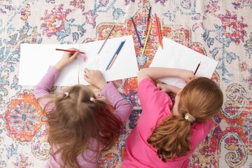 Cute kids learning to draw on floor at home, top view