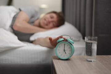 Happy man turning off alarm clock in bed indoors, selective focus