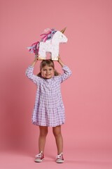 Happy girl with unicorn shaped pinata on pink background