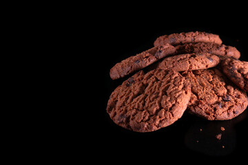 Close-up of tempting sweet chocolate chip cookies arranged on a dark surface and background. Suitable for promotions, and culinary concept content.