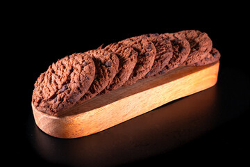 Sweet chocolate chip cookies are arranged in rows on wood and placed on a black surface and...
