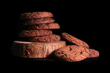 Stack of sweet chocolate cookies on wood on black surface and background, perfect for advertising,...