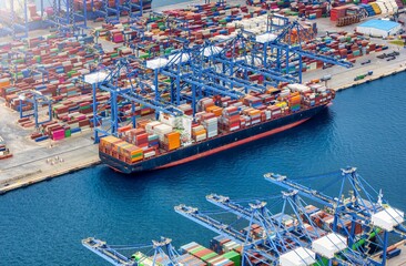 Aerial view of a large container cargo vessel being loaded and unloaded by cranes in a commercial terminal harbour