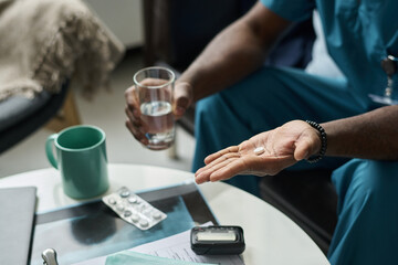 Close-up of medical professional holding glass of water in one hand and pills in other hand while sitting at table