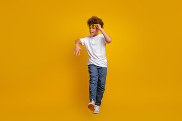 Stylish young boy posing against a yellow background with sunglasses showcasing a modern casual...