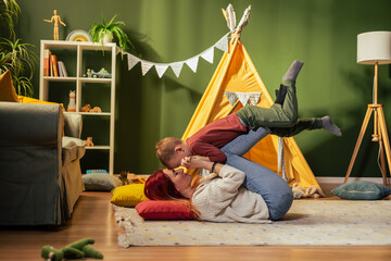 Mother lying on floor playing with son in cozy playroom