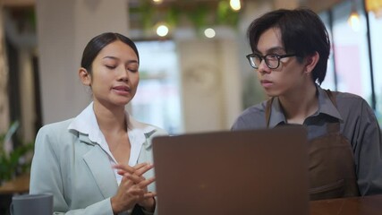 Young asian female manager explaining task to restaurant staff, using laptop to show information, business coaching or team training in coffee shop, communication between supervisor and employee - Powered by Adobe