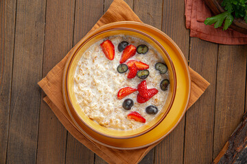 Portion of sweet breakfast oatmeal porridge with berries on wooden background