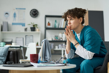 Medical professional wearing scrubs contemplating in a modern clinic setting, with stethoscope and...