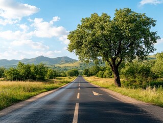 Naklejka premium Serene rural road lined with trees and mountains in the background