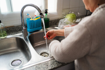 Elderly woman washing fresh radishes under running water in her kitchen sink, embodying healthy eating habits