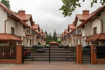 Gated entrance to private territory with standardized design townhouses in rows. Secure inner area fostering a close knit community feel. View of orderly suburban living, shared neighborhood spaces.