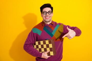 Cheerful young man in colorful sweater wearing retro glasses posing with a checkered box against a...