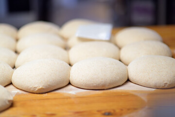 A batch of formed dough pieces on a table in the kitchen of a local bakery ready to bake. Olive ciabatta blanks laid out in a row in front of a large oven. Local bread production