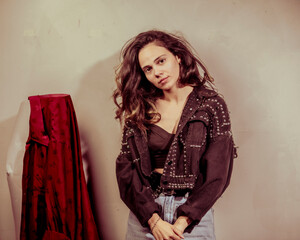This portrait captures a thoughtful woman posing in a fashionable jacket with embellishments,...