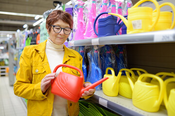 Portrait of elderly woman during shopping at mall. Red-haired elderly lady chooses a watering can at a home and garden goods store.