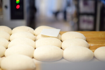A batch of formed dough pieces on a table in the kitchen of a local bakery ready to bake. Olive ciabatta blanks laid out in a row in front of a large oven. Local bread production