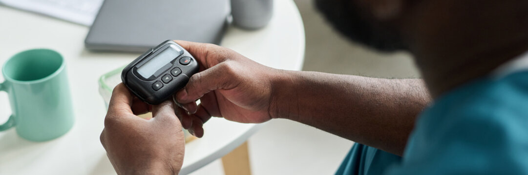 Person holding pager with both hands while sitting at table with cup and laptop in background, focused on device