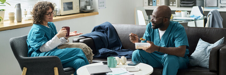 Medical professionals engaging in a conversation during a break in hospital lounge, sharing a meal and beverage, indicating camaraderie and teamwork