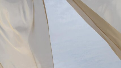 Light breezy sheer curtain blowing in the wind with cloudy sky behind it