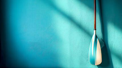 Modern racing kayak paddle leaning on turquoise wall in sunlight with strong shadow, perfect for sports branding, summer activity gear and water sports visuals