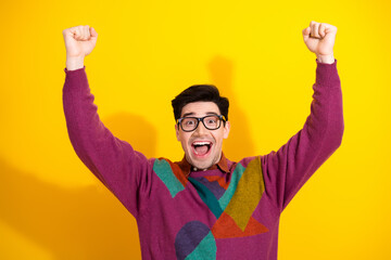 Excited young man in stylish sweater and glasses celebrating success against a vibrant yellow...
