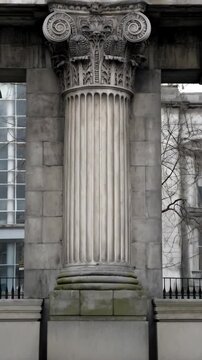 Elaborate architectural column featuring fluted shaft and ornate Corinthian capital with volutes and acanthus leaf details, stone texture.