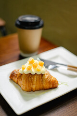 Freshly baked croissant topped with cream and fruit served next to coffee in a cozy cafe setting