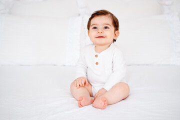 a baby on a white bed at home, a place for text, a cute smiling little child getting ready for bed, a portrait of a little boy child