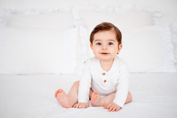 Fototapeta premium a baby on a white bed at home, a place for text, a cute smiling little child getting ready for bed, a portrait of a little boy child