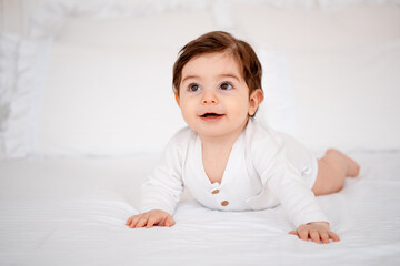 Fototapeta premium a baby on a white bed at home, a place for text, a cute smiling little child getting ready for bed, a portrait of a little boy child