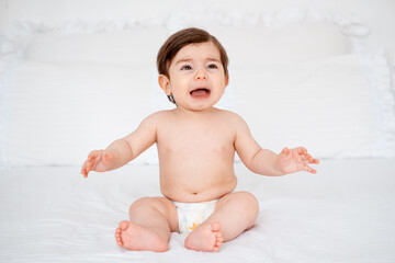 A crying baby on a white bed at home, a place for text