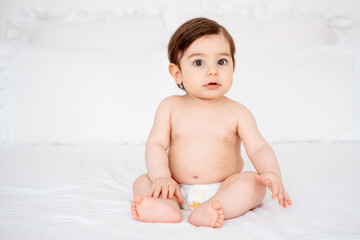 A baby in diapers on a white bed at home, a place for text, a cute smiling little child