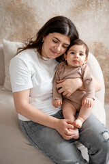 baby and mother, mom hugging baby at home, maternal love and care, mom with a small child, brown or beige background