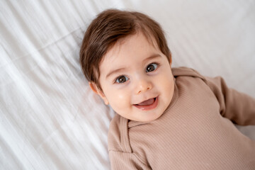 a baby, a close-up portrait of a smiling or laughing baby boy on a white bed, a place for text