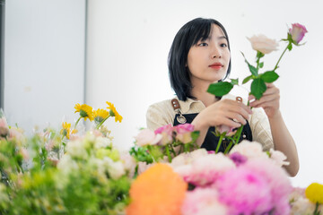 Woman arranging fresh flowers in a bright room filled with colorful floral arrangements during the...