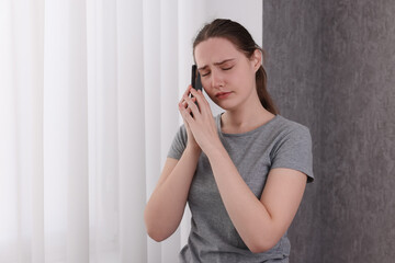 Stressed woman calling hotline for mental health help near window at home. Space for text