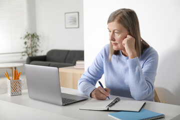 Woman learning online using laptop and taking notes at table indoors. Self-study