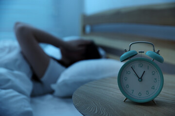 Frustrated young woman suffering from insomnia on bed indoors, focus on alarm clock