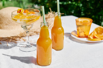 Cold summer drink. Refreshing fresh orange juice in bottles with drinking straw on the table in the garden.