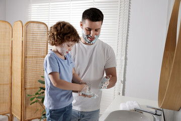 Happy father and his son with shaving cream on their faces in bathroom