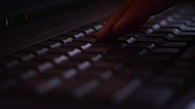Close-up of hands actively typing on a laptop keyboard in a dimly lit environment, suggesting focused work, coding, or late-night activity