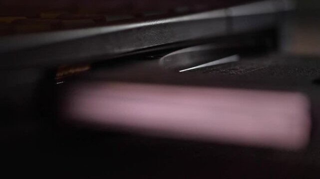 A close-up shot captures the precise and functional mood as a hand carefully inserts a CD into an older model laptop's optical drive, in a softly lit setting